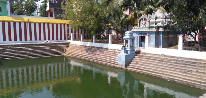 A green-watered temple tank with stone steps on both sides and a small shrine beyond.