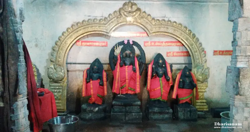 Four dark idols draped in red cloth under an arch with name boards