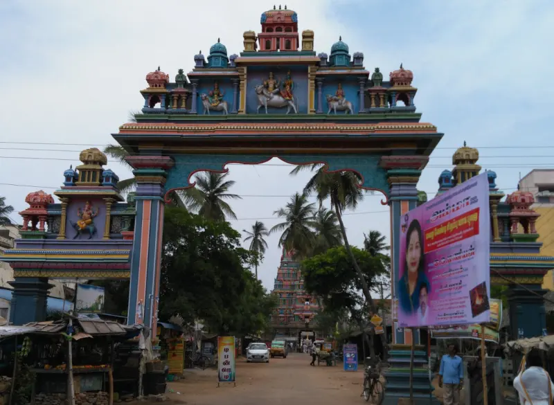 A tall painted arch over the road with figures on bulls, and the temple tower visible far beyond