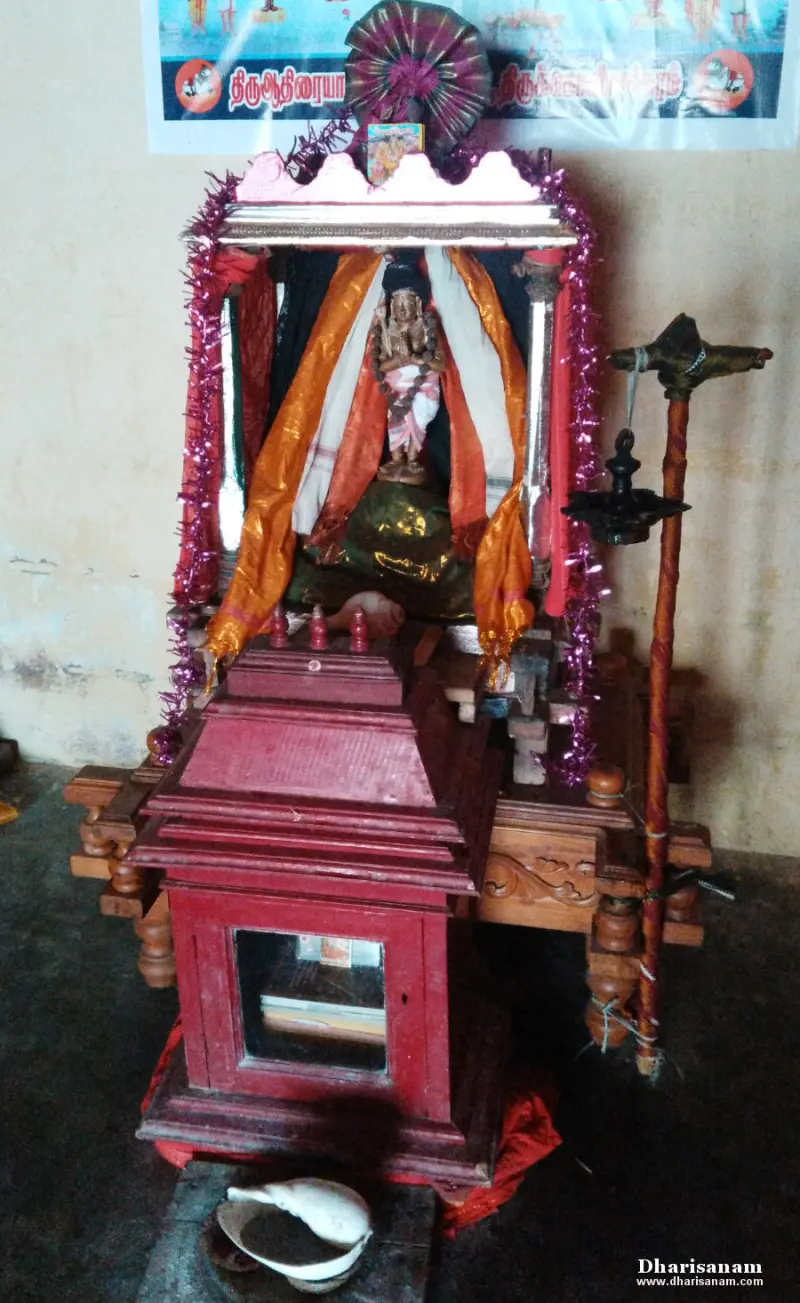 A small idol under cloth drapes on a decorated wooden stand, with a conch below.