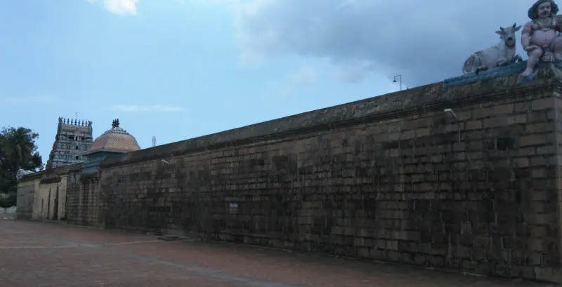 A long stone wall with a bull and figure on top, and towers in the distance