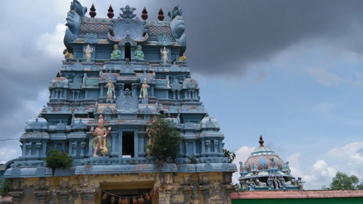 Blue and cream gopuram with stucco figures on its tiers, a small dome beside it under a cloudy sky