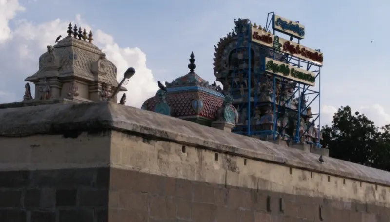 Small shrine towers behind a stone wall, with a blue frame carrying a temple name board