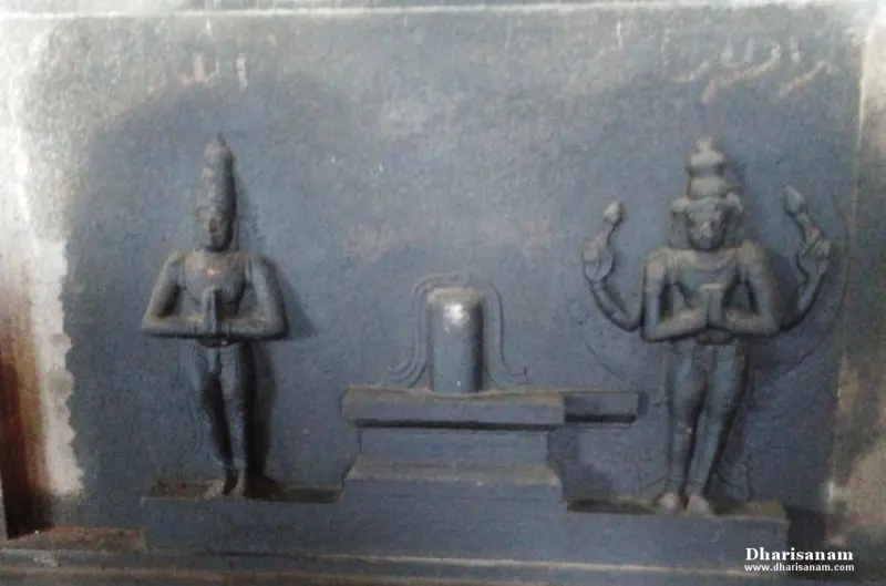 Dark stone relief of a lingam with a standing figure with folded hands on each side