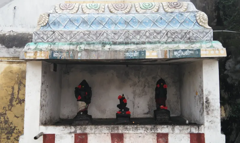 Three small black idols with red flowers in a white shrine