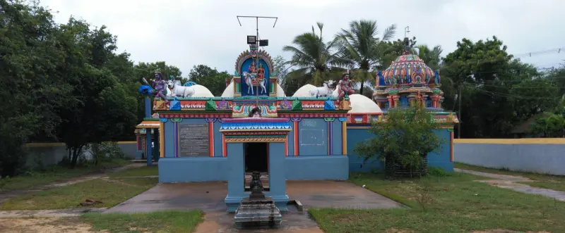 A blue shrine with white bulls on its roof, a Nandhi pillar in front and a tower beyond