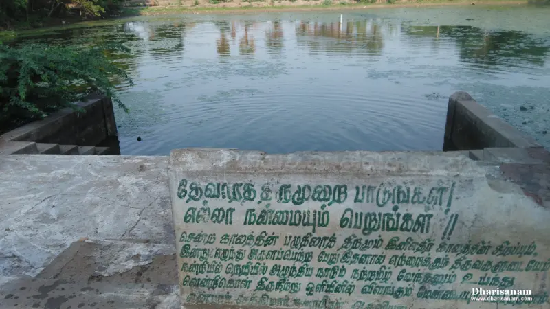 Still green water of a tank seen from a stone landing, with Tamil words painted in green on the wall of the steps