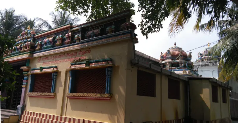 Cream temple hall with lattice windows and a painted tower behind