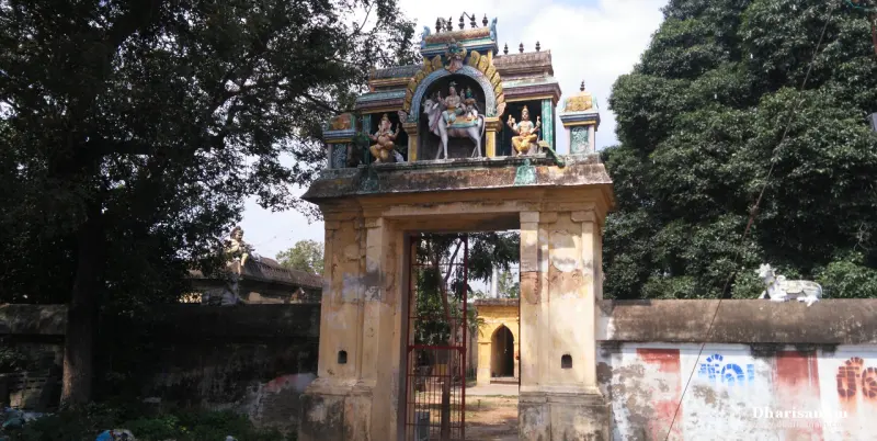 A weathered gateway with painted sculptures above the opening, a bull on the wall at right and big trees behind