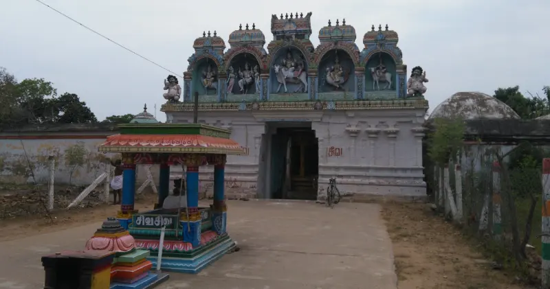 A gateway with painted figures above, and a small colourful pavilion standing in front of it.