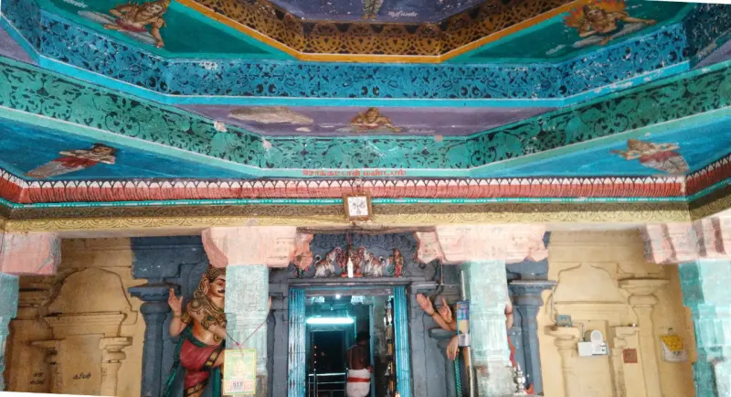 A hall with a painted green and blue ceiling above a pillared doorway; a man stands inside, guardian figures flank it.