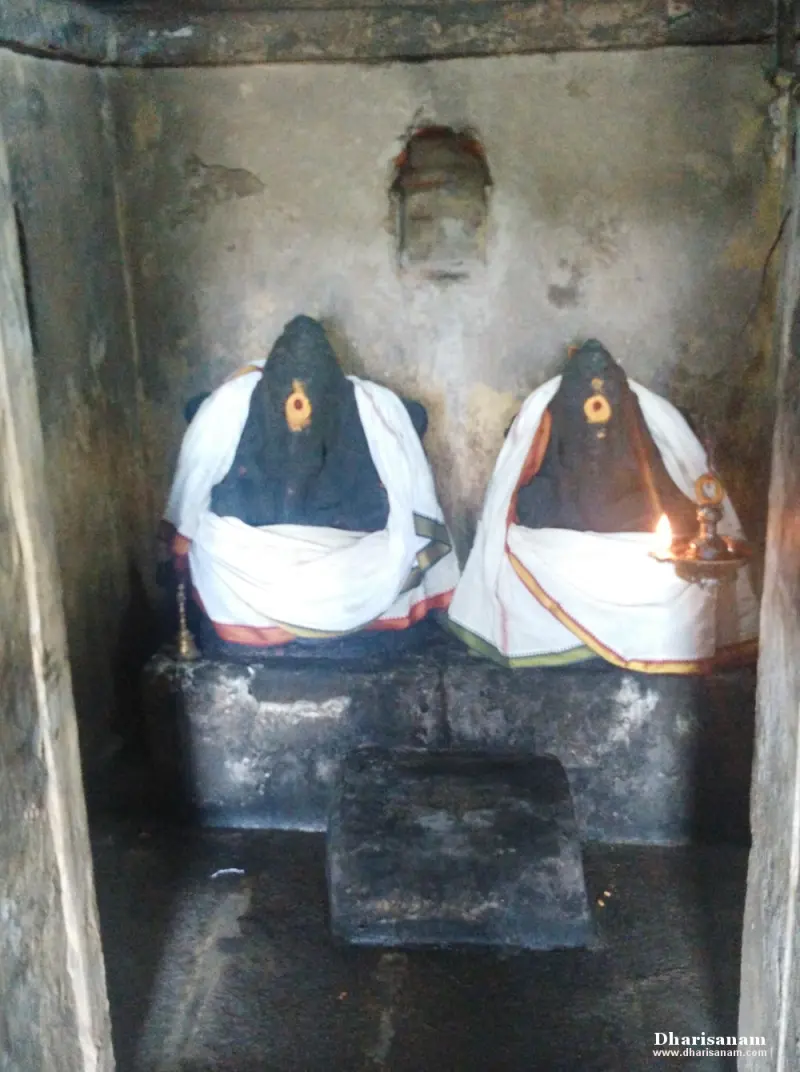 Two Vinayakar idols side by side on a stone platform, wrapped in white cloth, with a lamp.