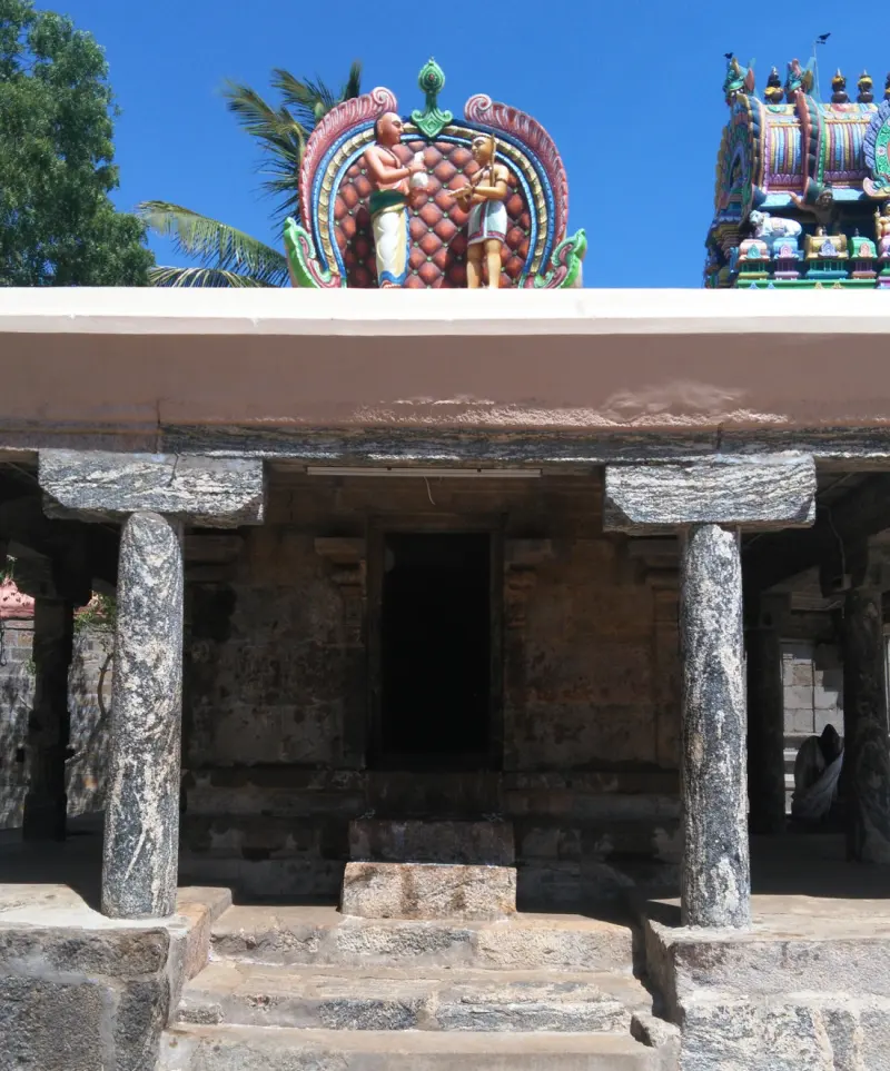 A pillared stone porch with steps and a dark doorway, and two painted figures on the roof above.