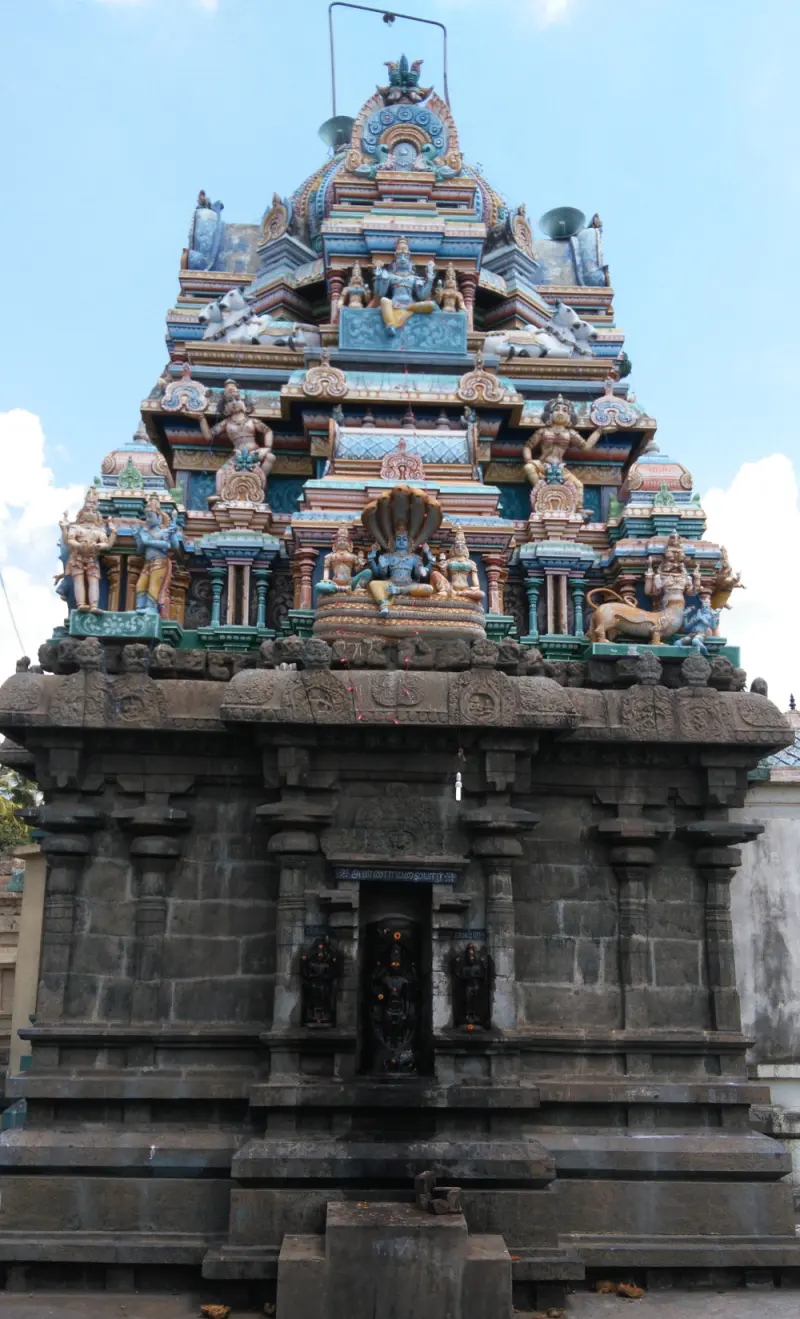 Stone-based shrine tower topped by many painted figures, under a blue sky