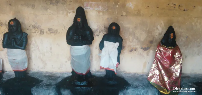 Four dark idols standing in a row against a wall, wearing white and red-and-gold cloth.