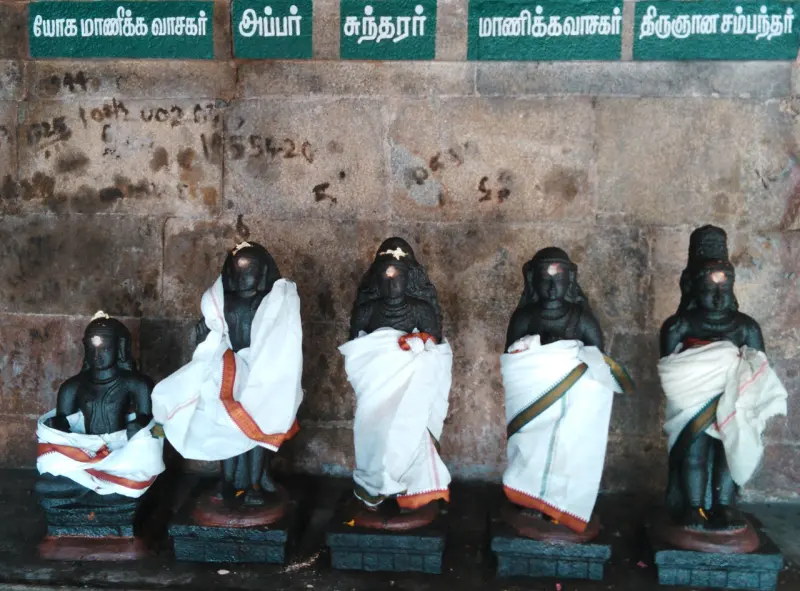 Five dark figures draped in white cloths in a row, with green name boards above them including Appar and Sundarar