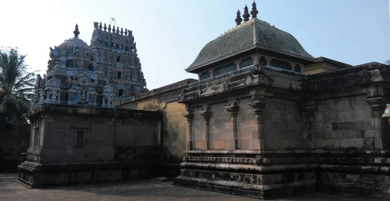 Stone shrines with a domed roof and a small colourful tower rising behind them, under a clear sky