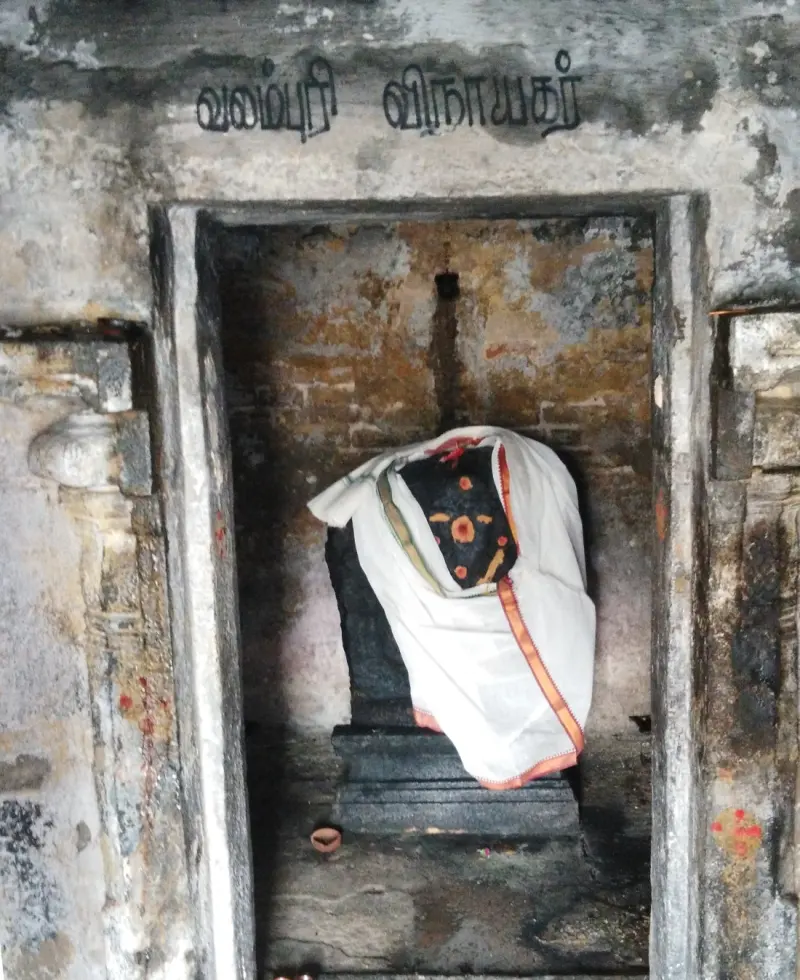 A small stone shrine with a Tamil name board above, holding a dark image draped in white cloth.