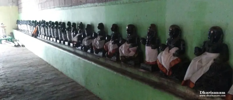 Many small dark seated idols in white cloth lined up on a ledge along a green wall in a corridor