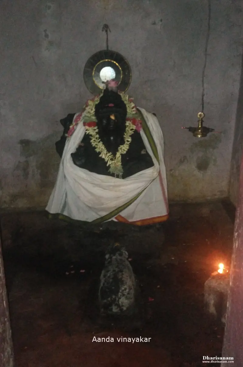 Garlanded black stone Vinayakar idol in a small chamber, with a lit lamp beside it