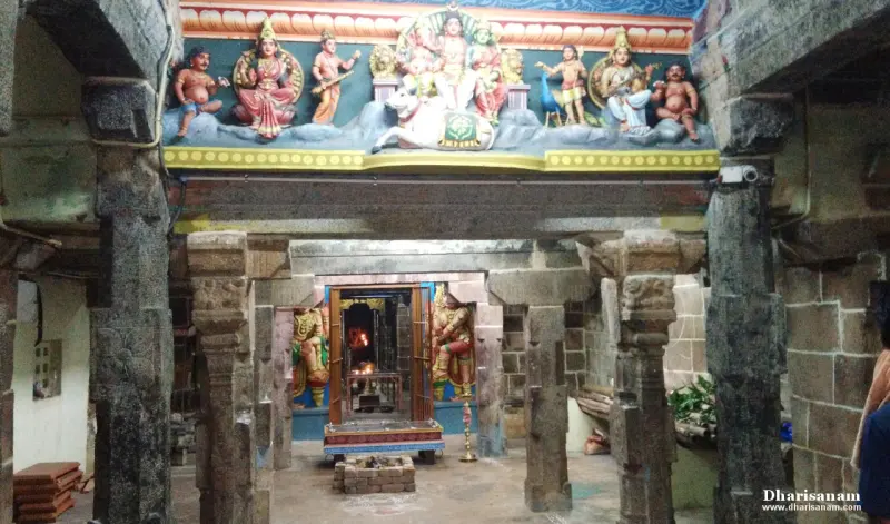 Stone pillars of a hall frame a lit shrine, with painted figures in a band above