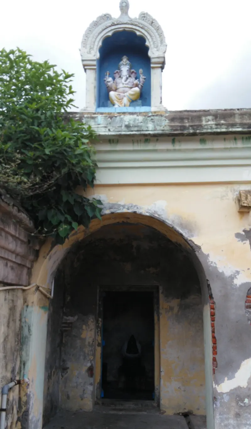 A stucco Vinayakar in a blue niche above an arched entrance to a dark inner shrine