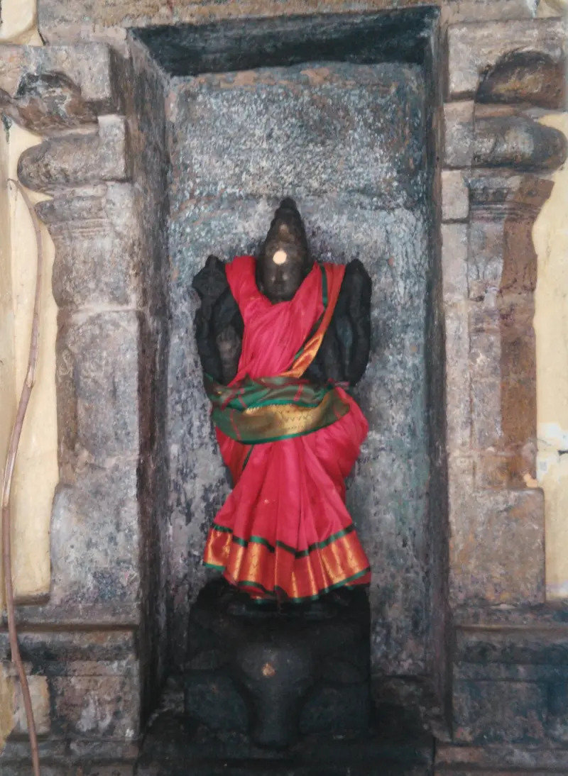 A black stone figure in a stone niche, wrapped in a red cloth with a golden border.