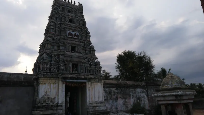 A tall carved gopuram above a whitewashed entrance, with a small domed pavilion at the right