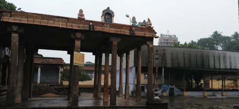 Stone pillars of a porch in the foreground, with a wide courtyard and buildings beyond.