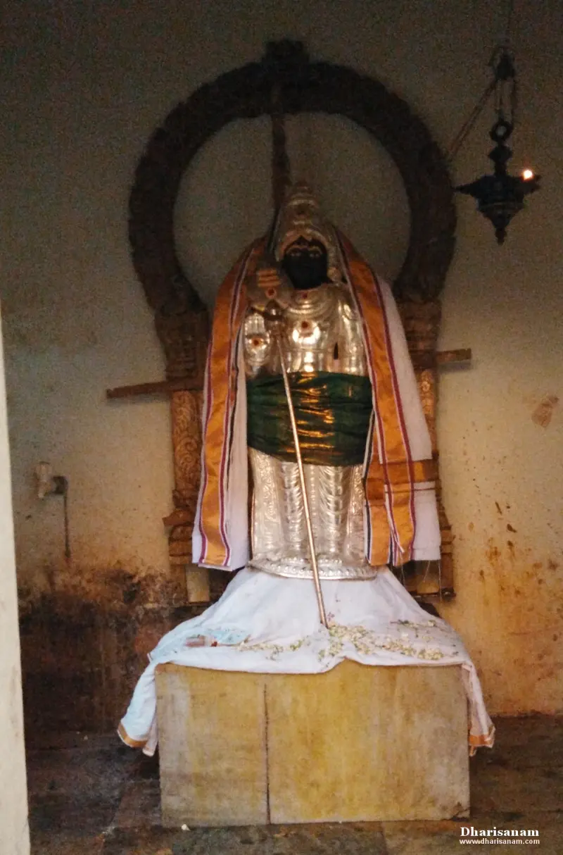 A standing idol in silver armour and a green waist cloth, holding a staff, on a stone platform