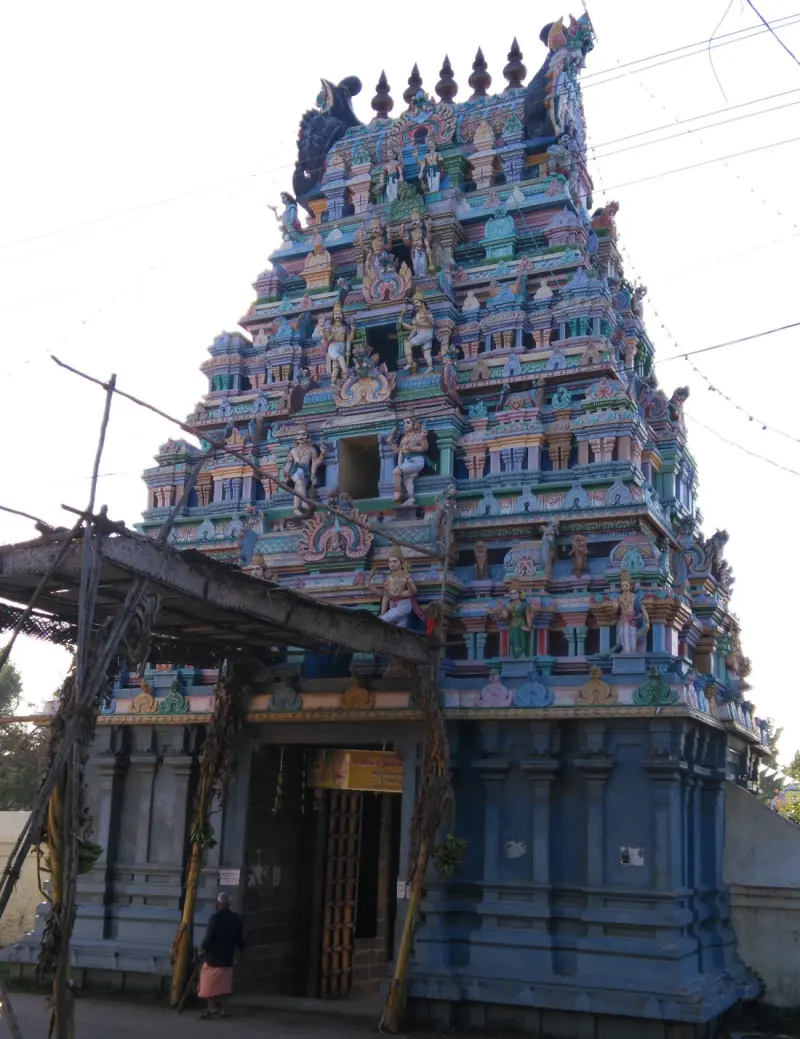 A tall tiered gateway tower with many painted figures over a blue base, with a person standing near the open door