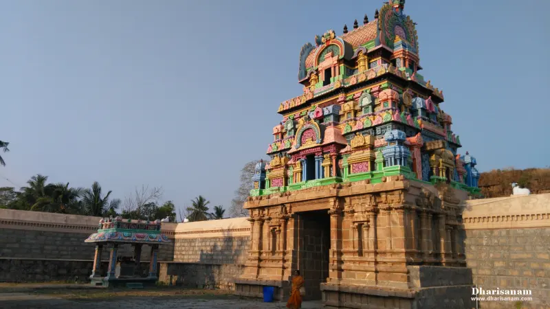 Painted gateway tower above a stone base, with a small shrine to its left and a person at the door