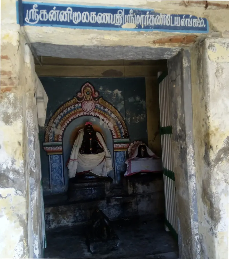 Narrow doorway under a blue Tamil board; inside, a dressed image in a painted arch and a lingam beside it