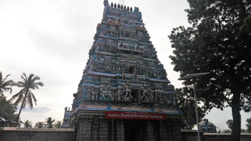 A tiered tower covered in figures above a dark gateway with a red name board, trees on the right