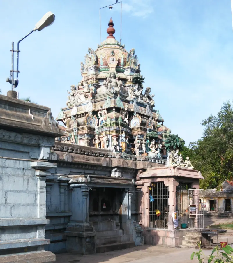 A multi-tiered painted tower crowded with figures, rising above a stone mandapam under a blue sky