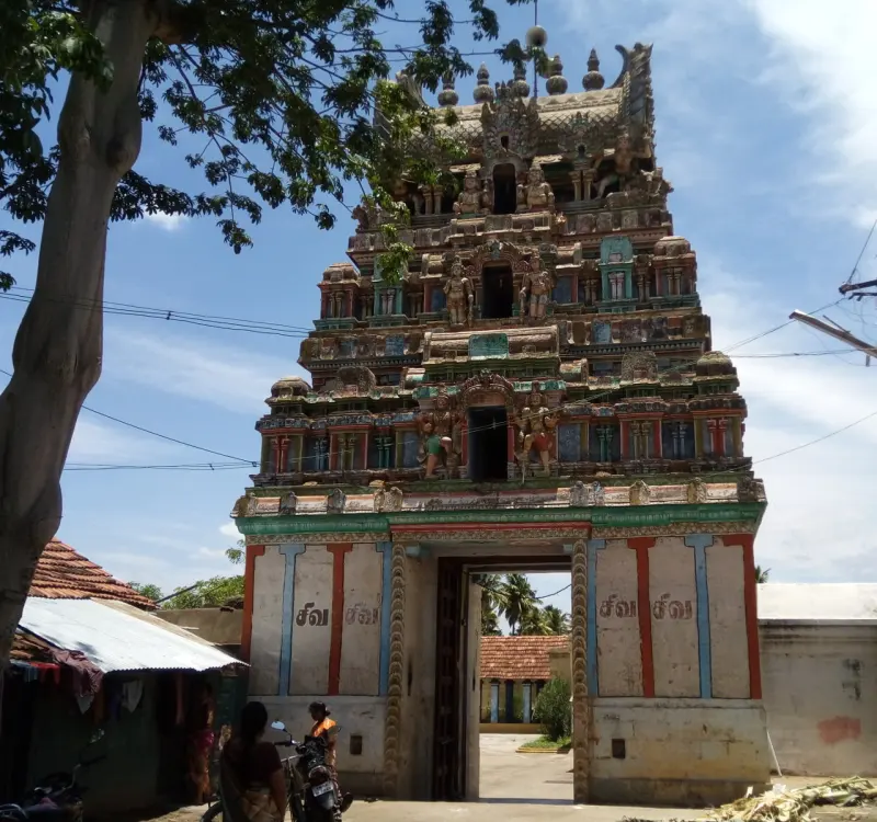 Tiered tower gateway with carved figures; a tree leans in at the left and two people stand below