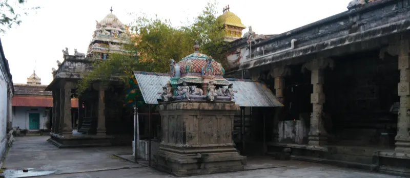 Small shrine with a decorated dome in a paved courtyard, towers beyond