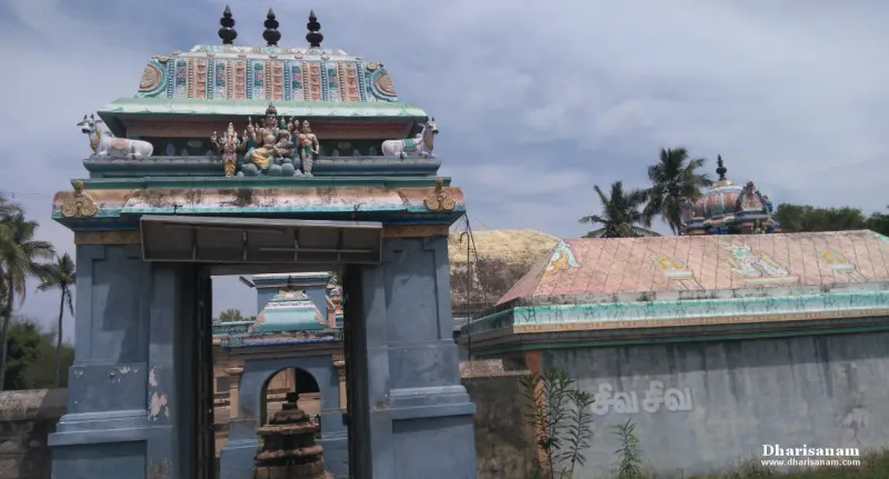 Blue gateway topped by a painted sculpture of two figures, with white bulls on its sides and another roof beyond