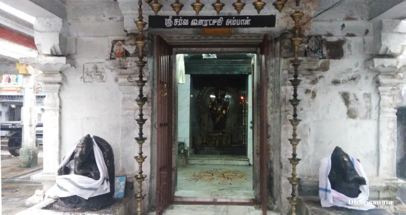 Shrine doorway with a name board, a deity inside and a black Vinayakar idol in white cloth on each side