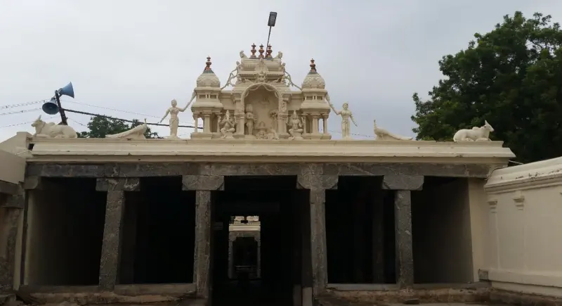 A pillared entrance hall with a small tower and Nandi figures on the roof, seen from outside under a cloudy sky.