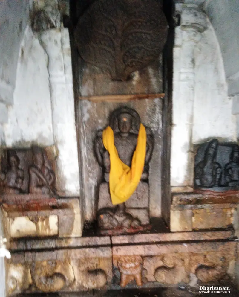 A stone idol with a yellow cloth stands in a niche beneath a large carved tree, with smaller reliefs on either side