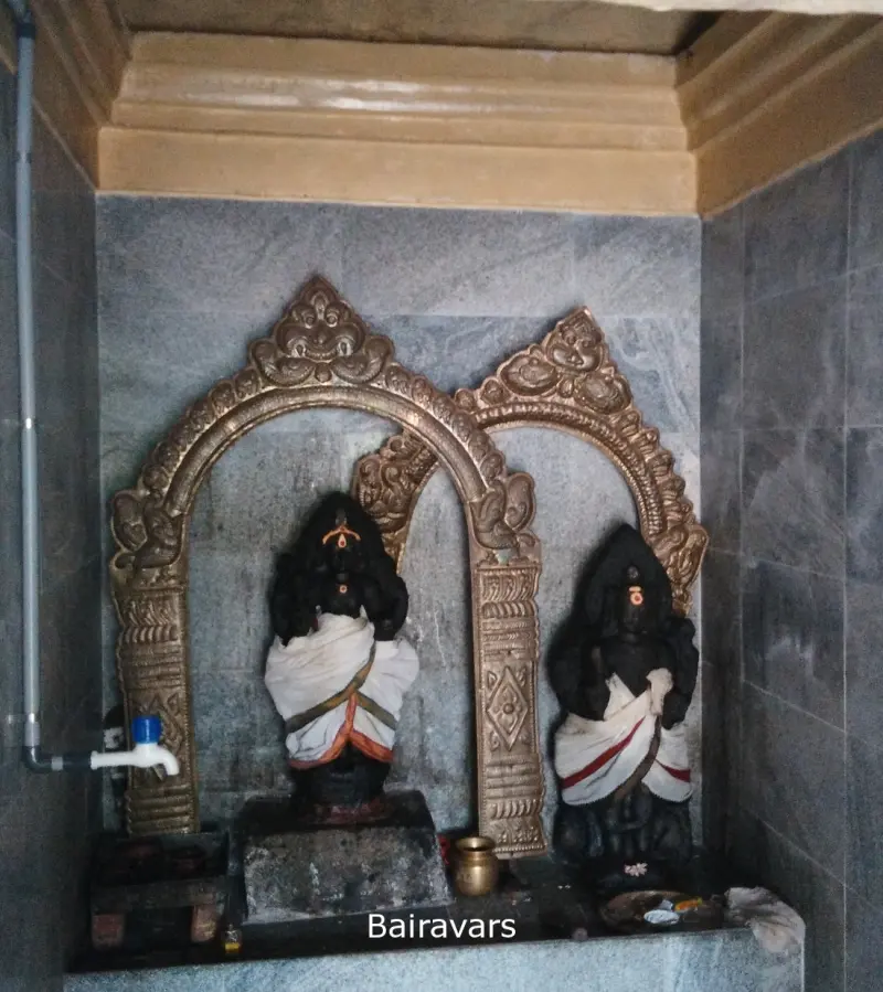 Two black stone idols in white cloth stand under metal arches, with a caption reading Bairavars.