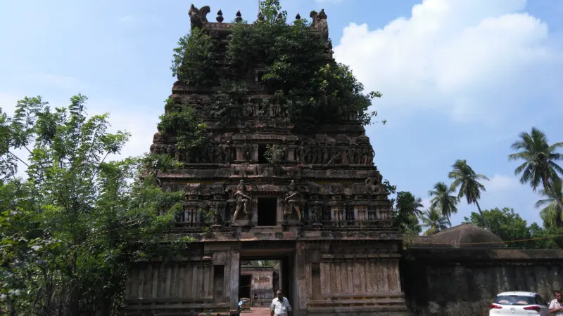 A tiered stone tower with figures on every level and green plants growing from the top, under a blue sky.