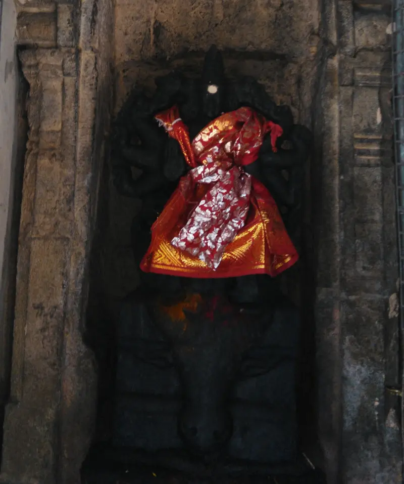 A dark stone idol in a wall niche, draped in an orange and red silk cloth with a white spot on its forehead.