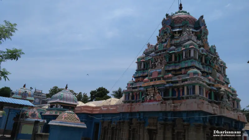 A tall painted tower rising from a blue structure, with small domed shrines in the foreground.