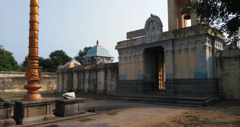 Tall copper-coloured flagstaff beside a gateway, with a shrine tower beyond the wall