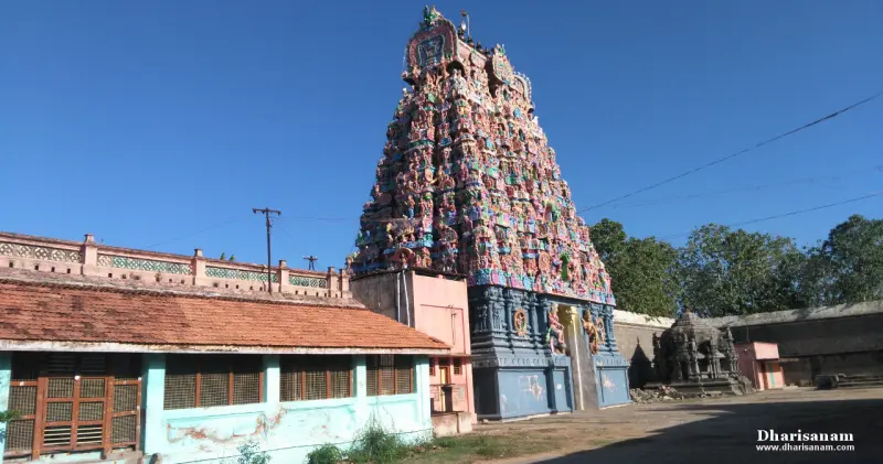 A tall painted tower beside a tiled-roof building under a blue sky.