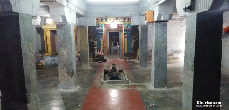 A hall of stone pillars with a red path leading past a Nandhi toward a lit shrine doorway at the far end