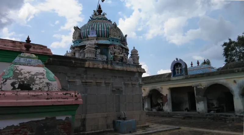 A stone-walled shrine topped by a green domed roof, with a pillared corridor to the right