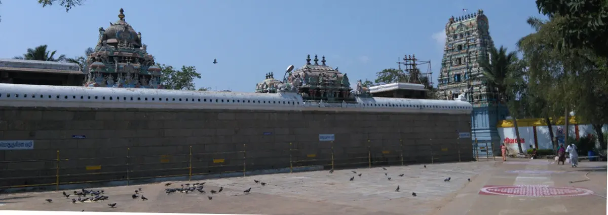 A long stone outer wall with temple towers behind it and pigeons on the paved ground in front.